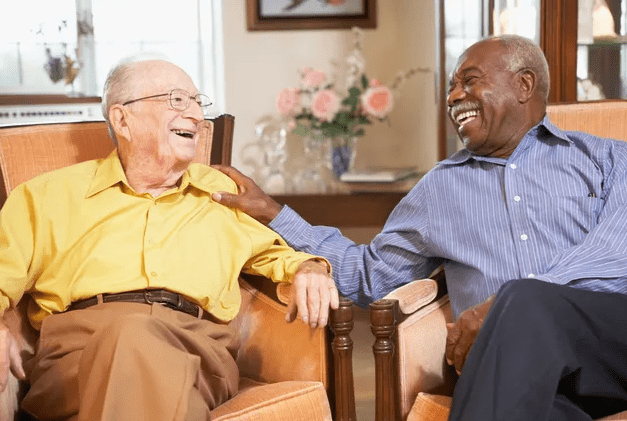 Two older men sitting on a chair and laughing.