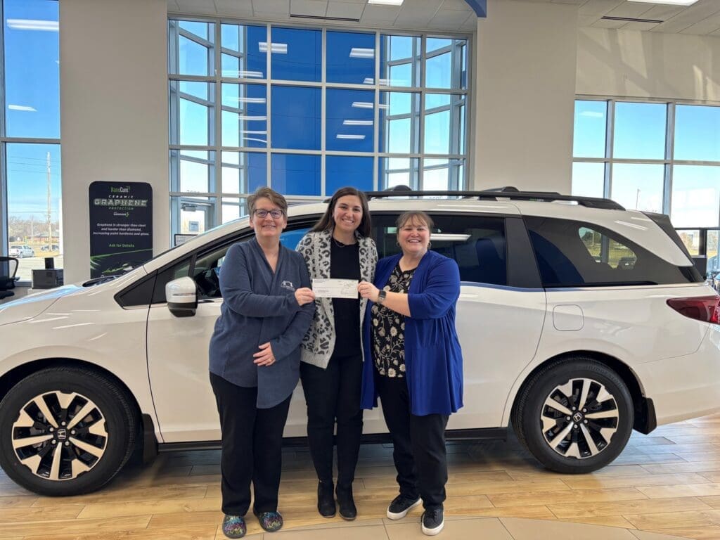 Three people holding check beside white SUV
